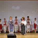 Daniela Toma alături de Ioana Anton, prezentatoarea spectacolului, pe scena Filarmonicii Pitești, cu Ansamblul „Mugurelul” din Costești în fundal
